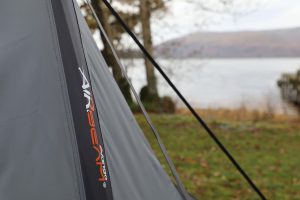 green polyester tent pitched on grass near waters edge