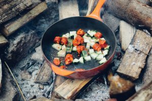 open campfire with a pan with cubed vegetables cooking