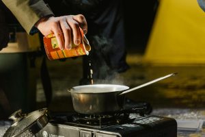 camping kitchen with steaming pan. man pouring a carton if liquid inside