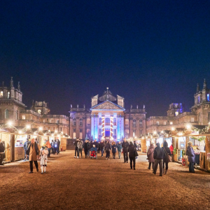 large stately home in background with Christmas chalets lining the edge. People bumbling around look at gifts